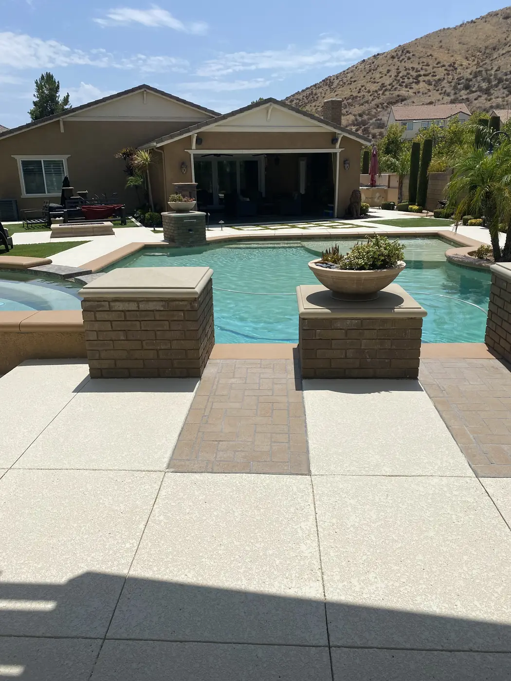 Wide backyard pool with a cream deck and brick planter walls behind a family home