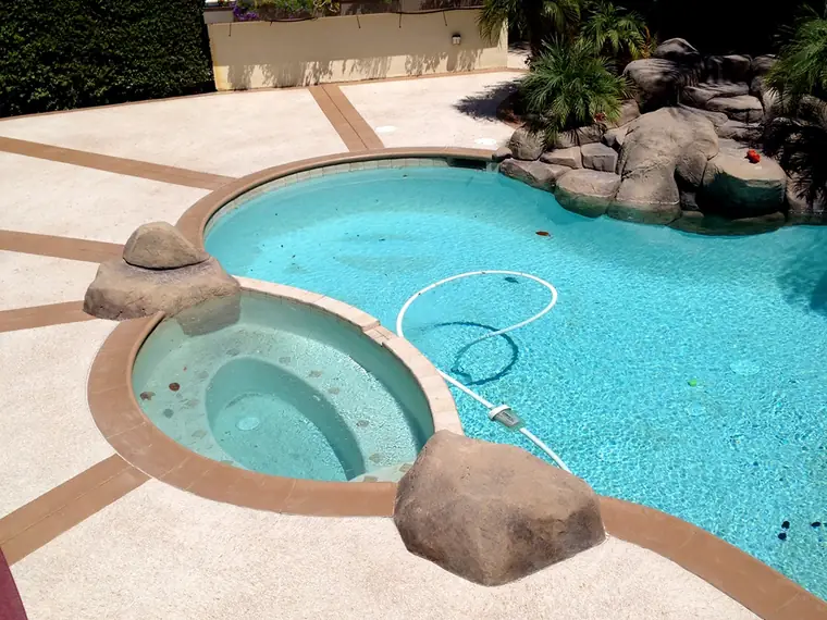 Backyard pool and raised spa surrounded by a tan textured cool deck