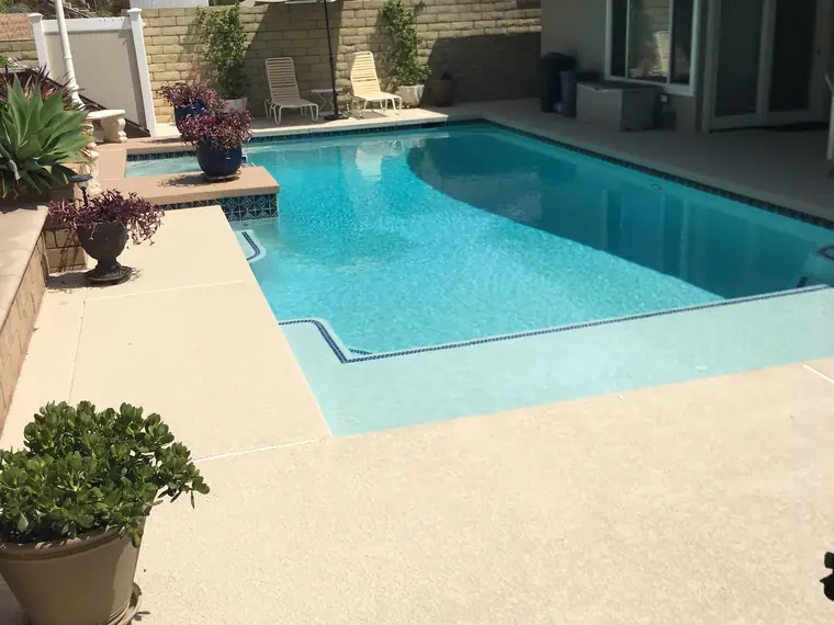 Curved backyard pool with a cream textured deck, fire pit and hillside view