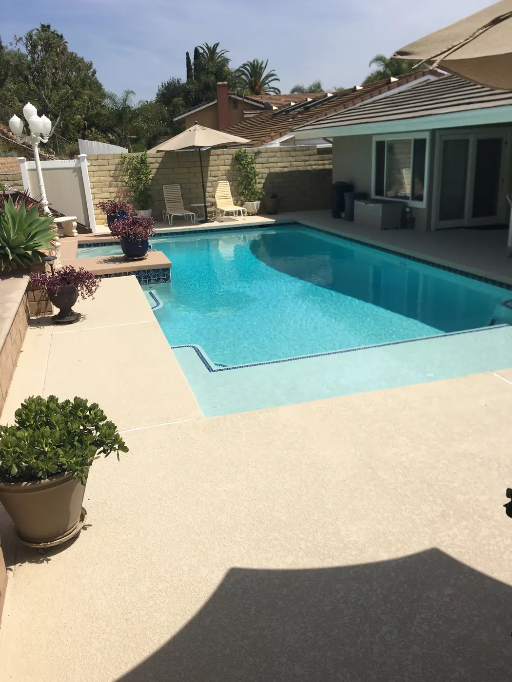 Curved backyard pool with a cream textured deck, fire pit and hillside view