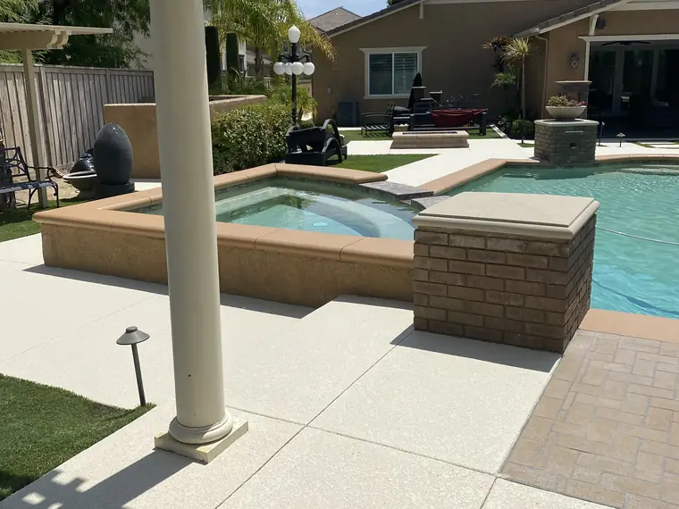 Pool and spa seen from a covered patio with a cream textured deck