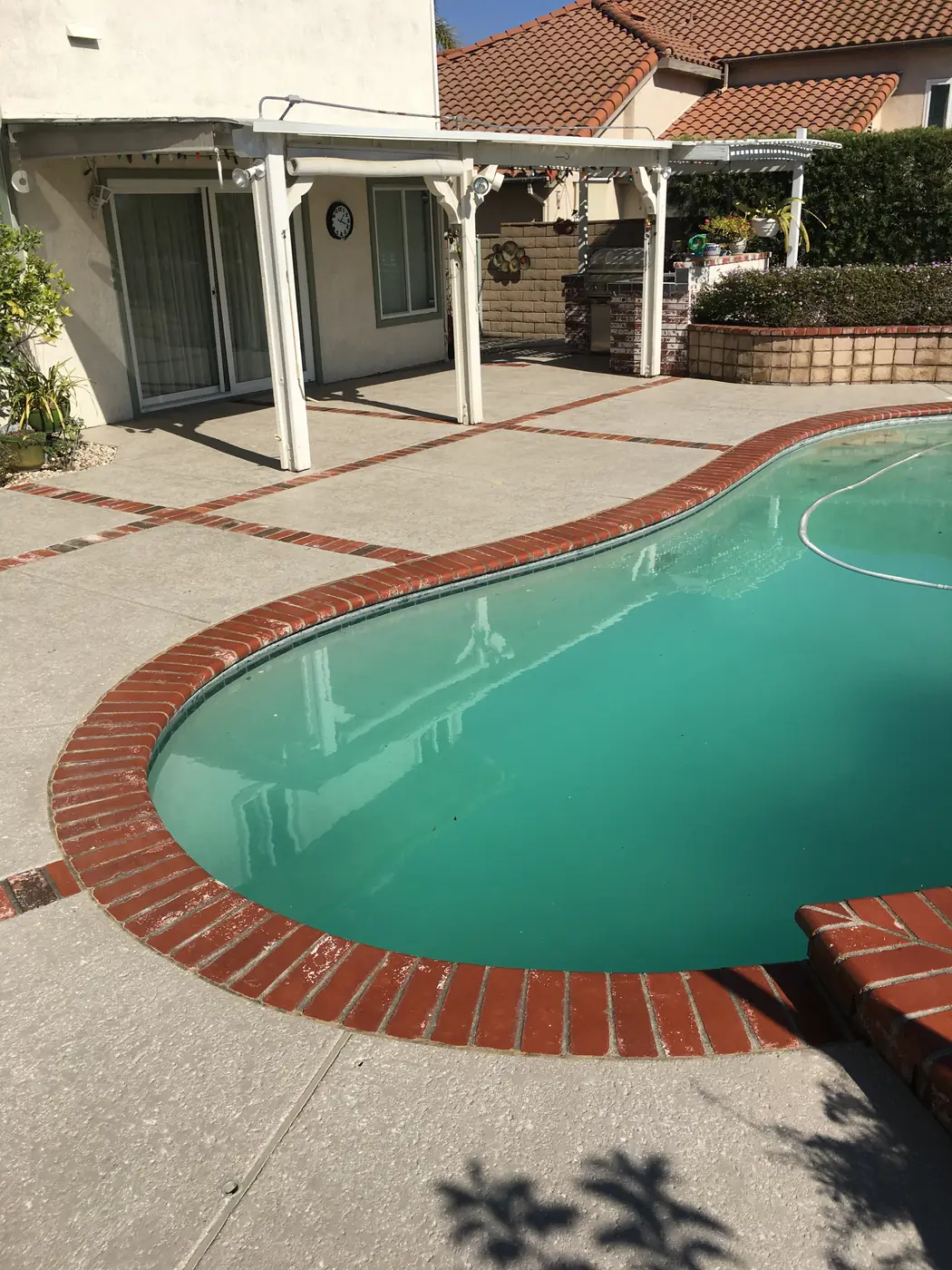 Kidney-shaped pool with red brick coping and a light gray textured deck