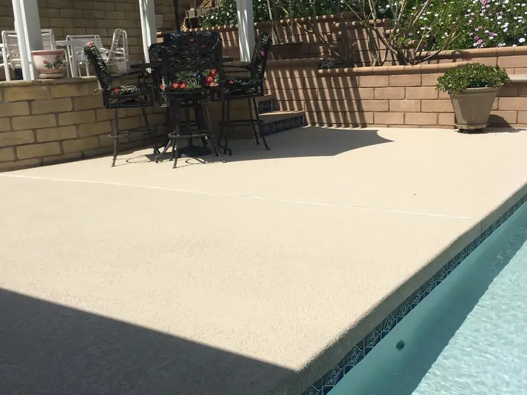 Patio furniture and umbrellas on a cream pool deck beside a backyard pool