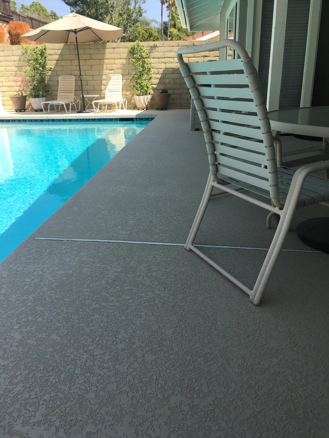 Poolside chairs on a gray textured deck beside clear blue water