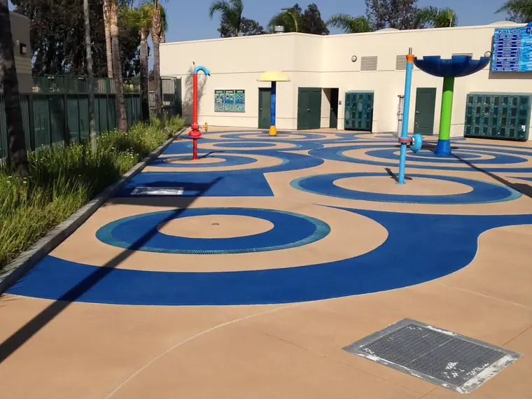 Blue swirl splash pad set into a tan deck outside a community building