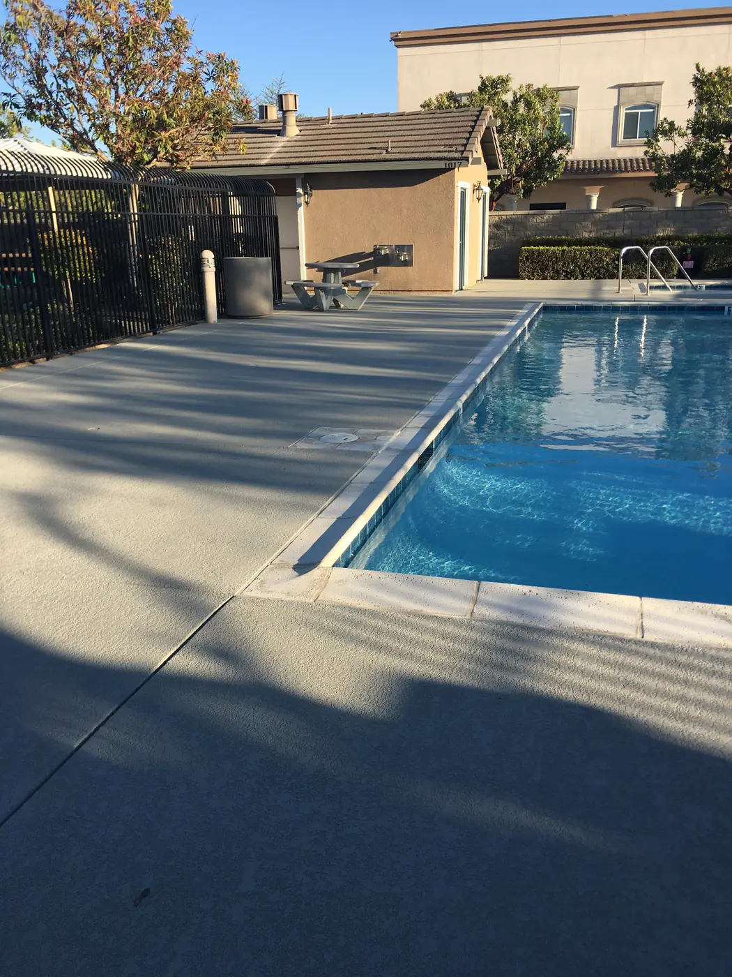 Pool with a gray textured deck and long evening shadows
