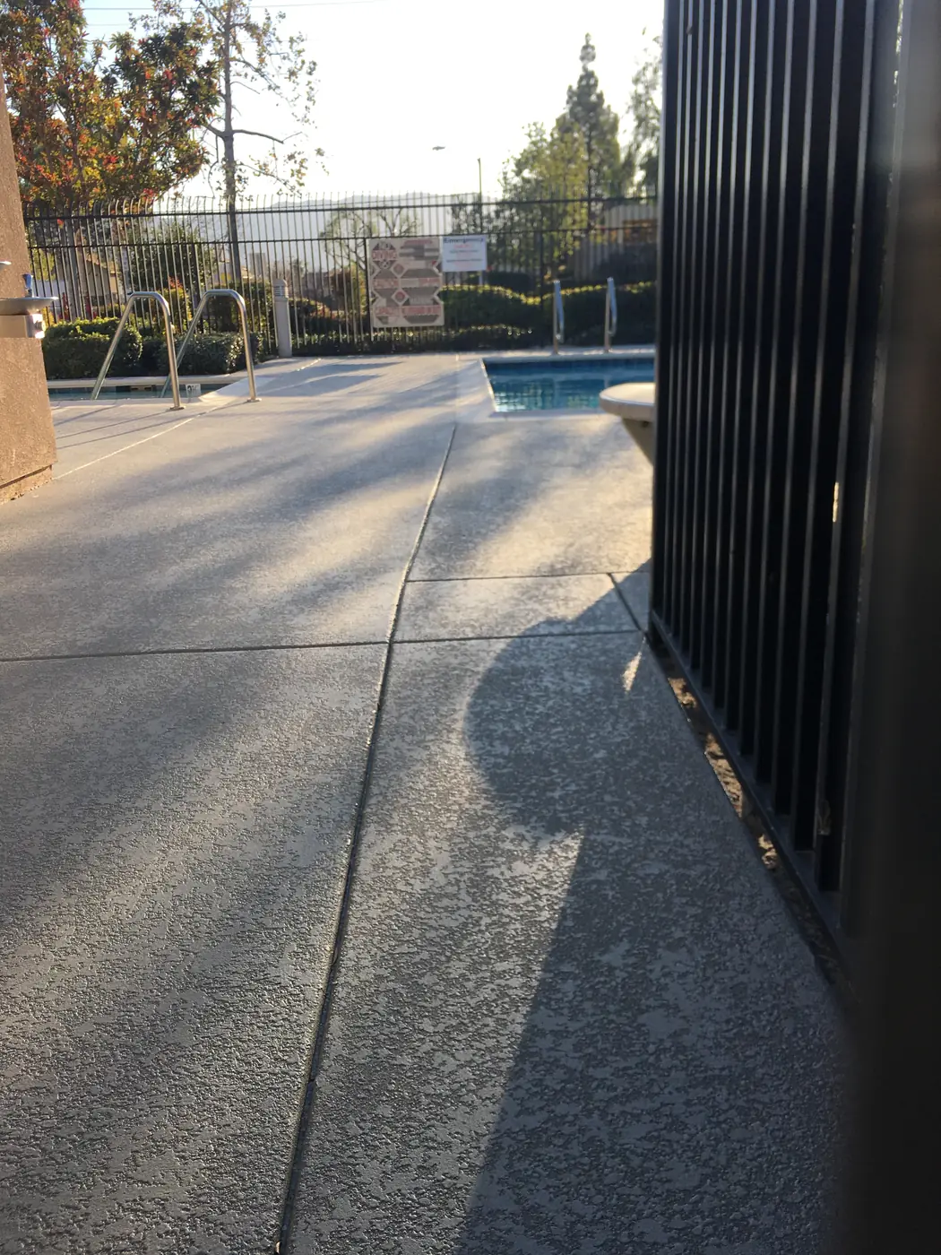 Gray speckled pool deck seen past a black metal fence