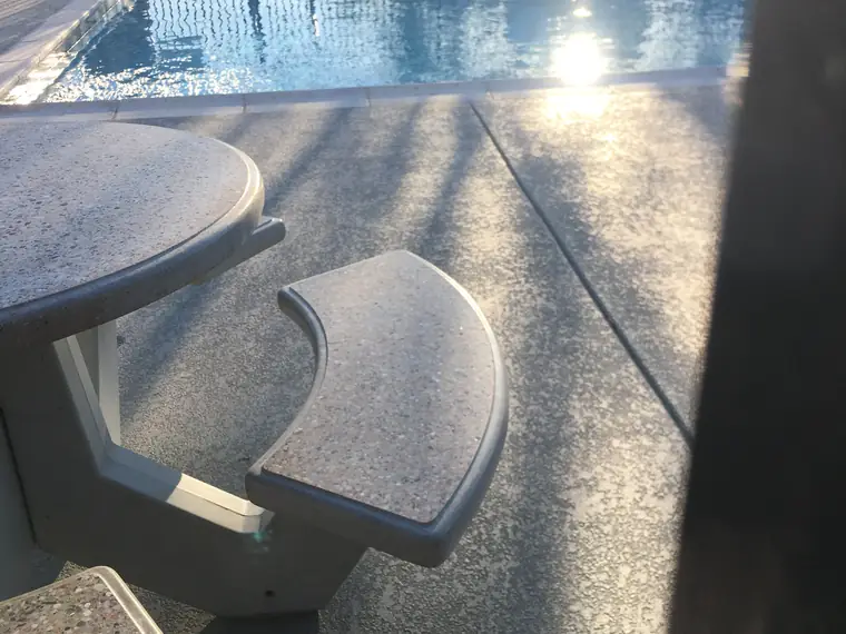 Concrete table and benches on a speckled gray pool deck