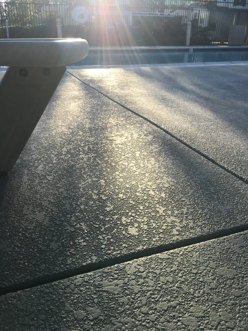 Textured gray deck lit by low sun beside a pool
