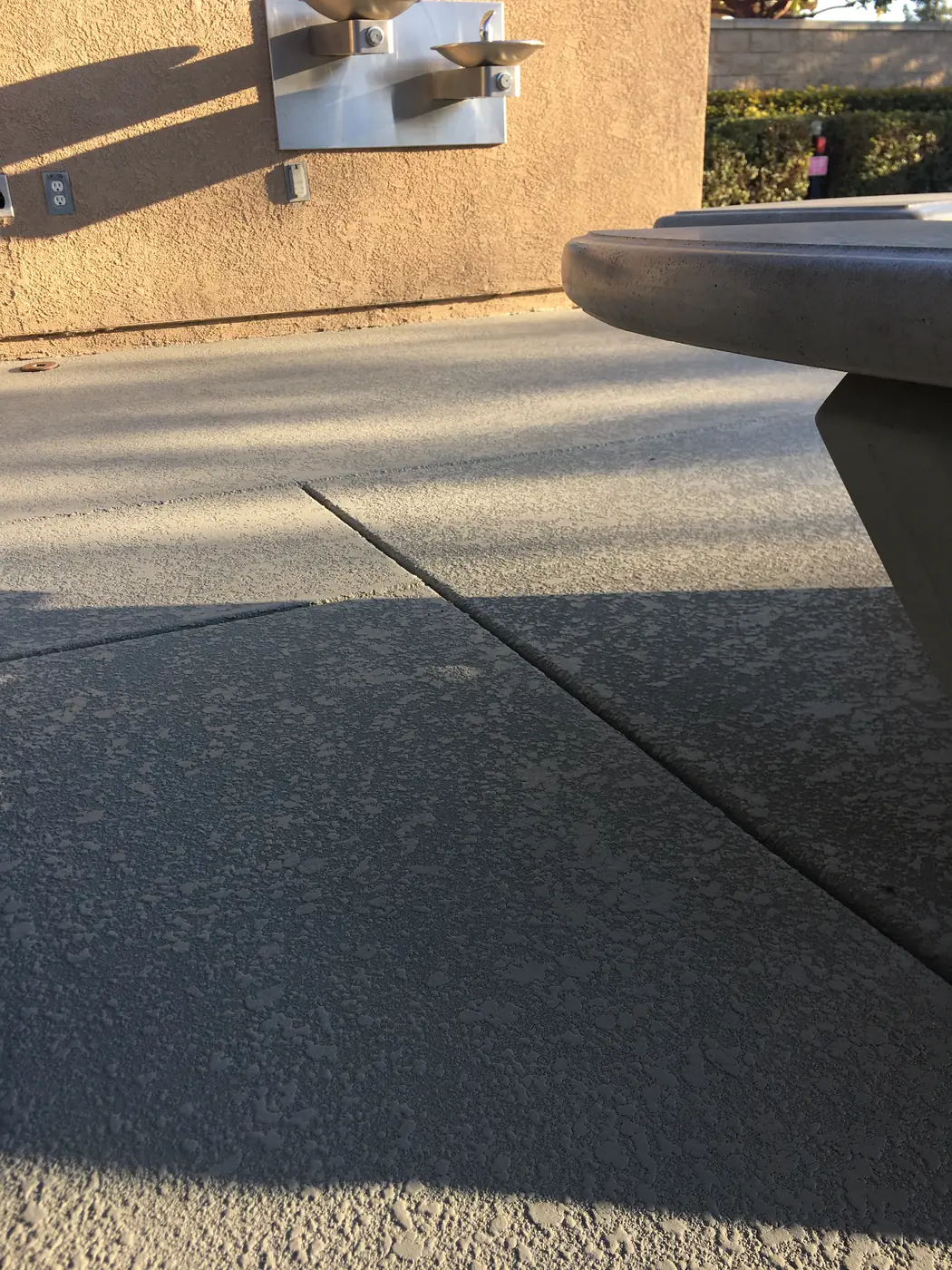 Gray textured pool deck with a concrete table at the edge of frame