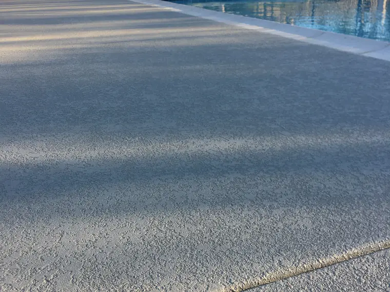Gray textured deck running alongside a commercial lap pool
