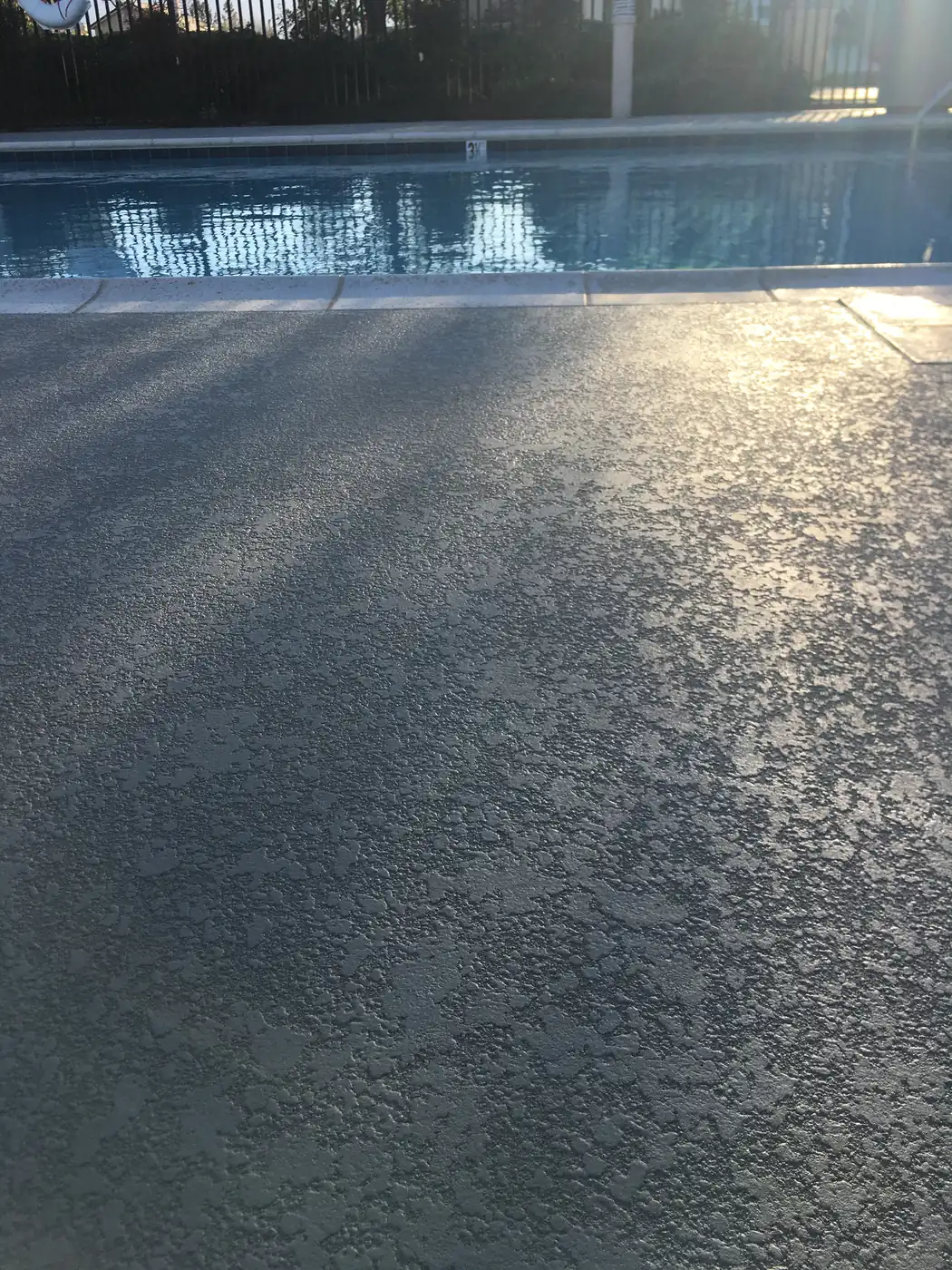 Gray pool deck with sunlight and shadow across the textured surface