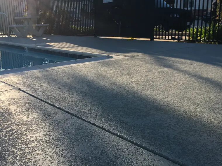 Gray textured pool deck behind a black fence at a community pool