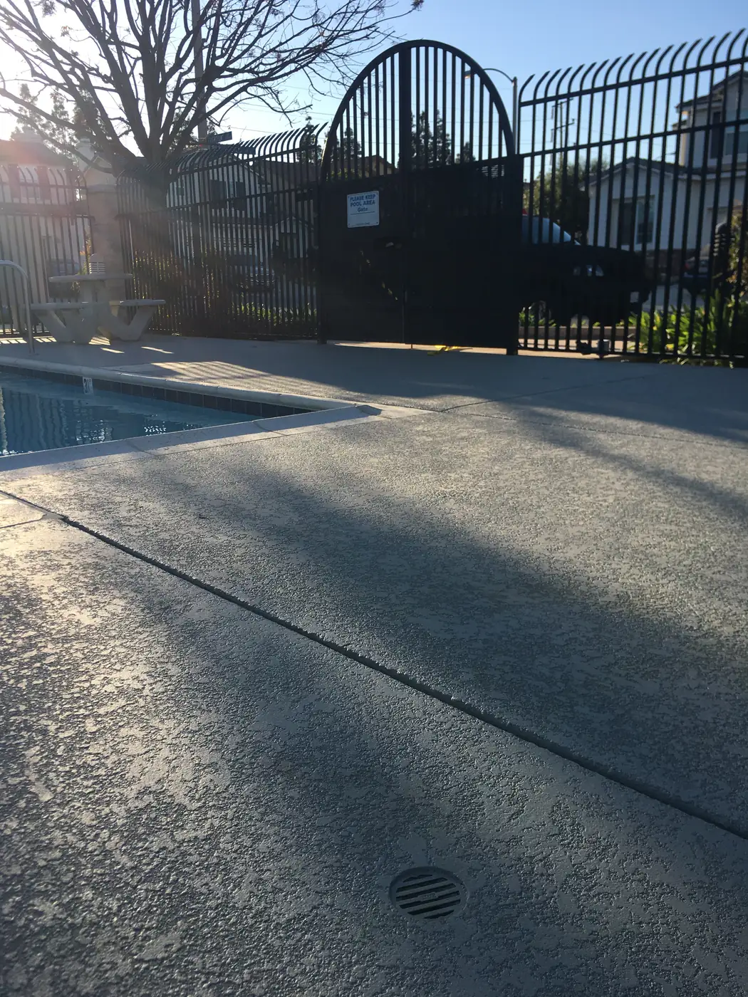 Gray textured pool deck behind a black fence at a community pool