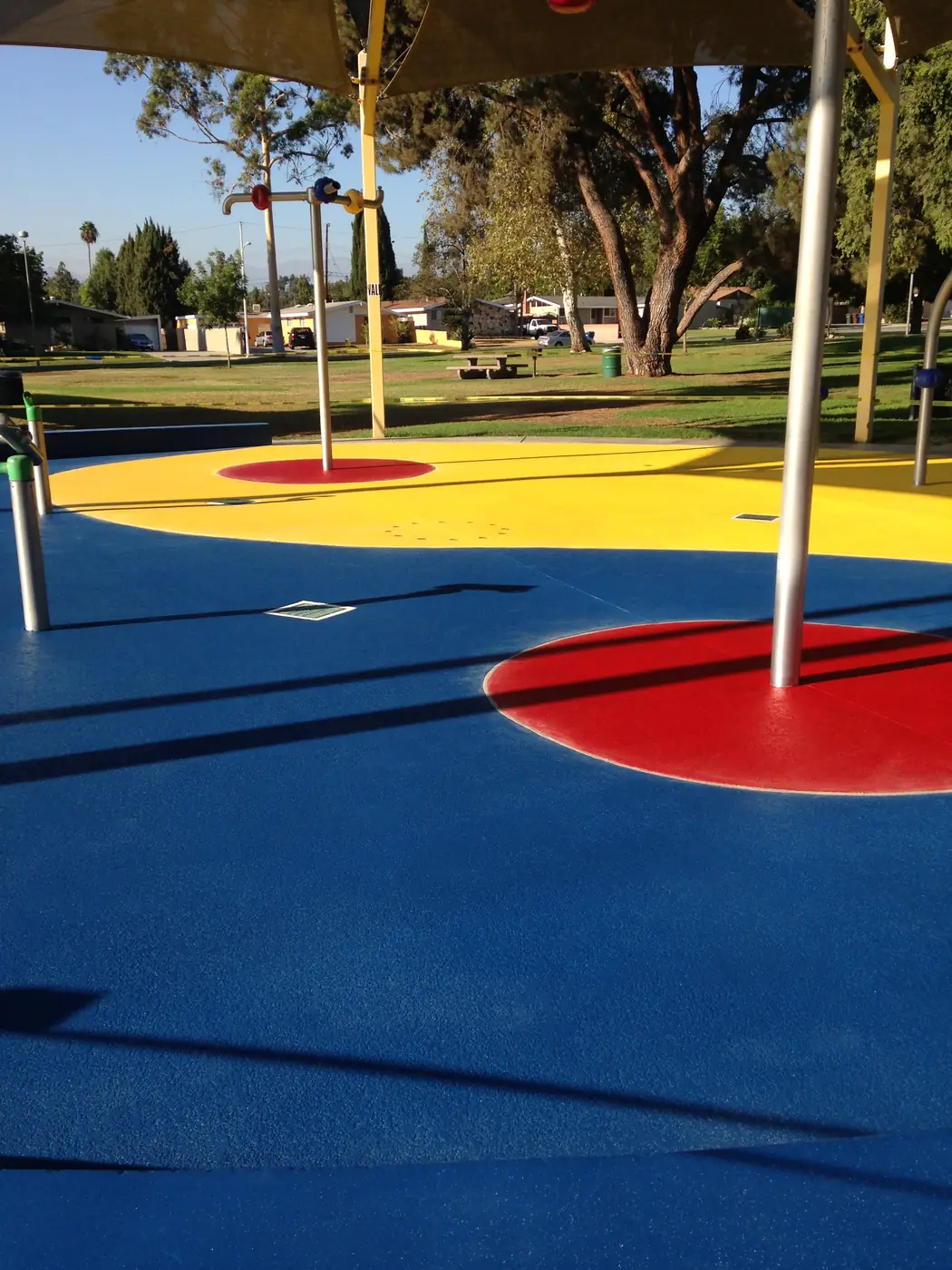 Blue and yellow splash pad in a park with a red circle and play posts