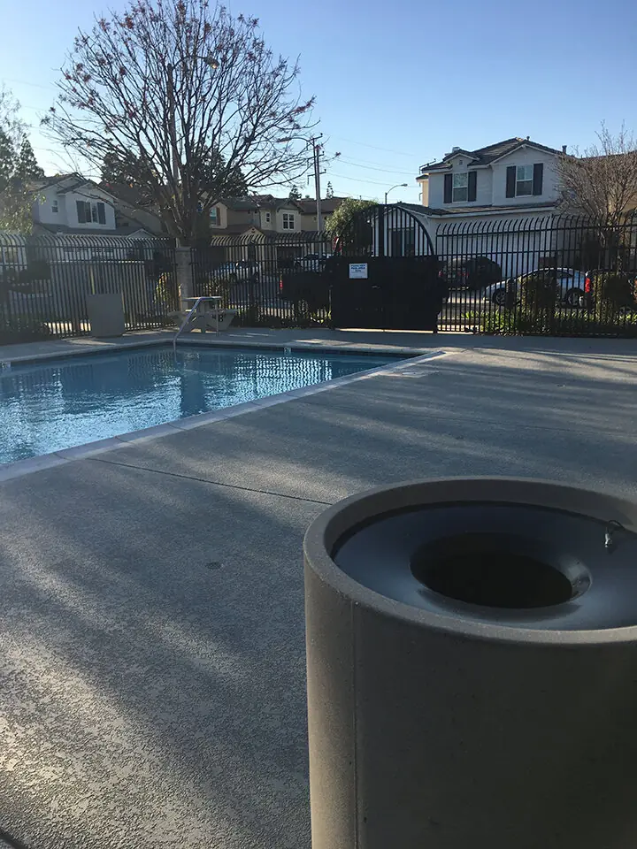 Apartment complex pool with a gray textured deck and metal fencing