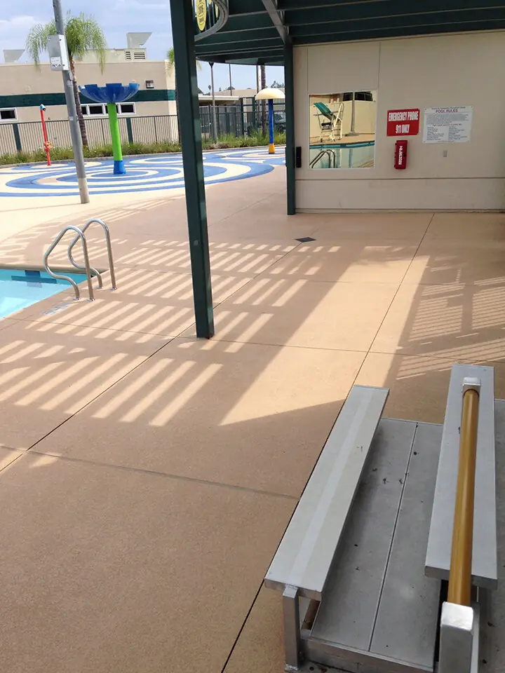 Tan pool deck running under a shade structure at a community pool