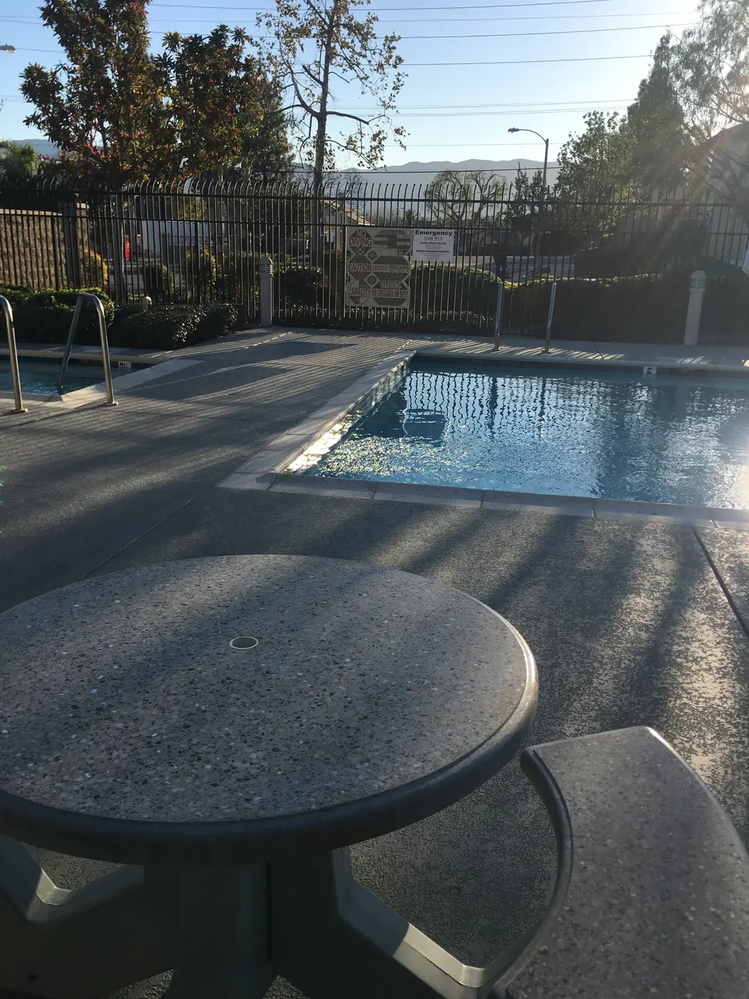 Concrete table and stools on a gray textured pool deck with a blue-gray border beside a community pool
