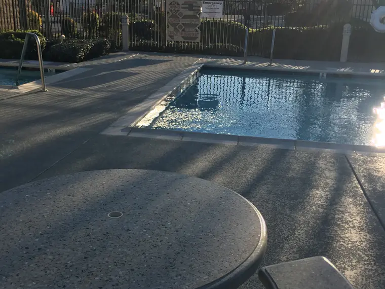 Gray textured deck and blue-gray border band running to a pool in low afternoon sun