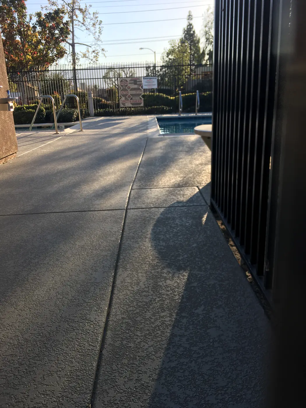 Gray resurfaced walkway with a blue-gray edge band leading past a black fence to a pool