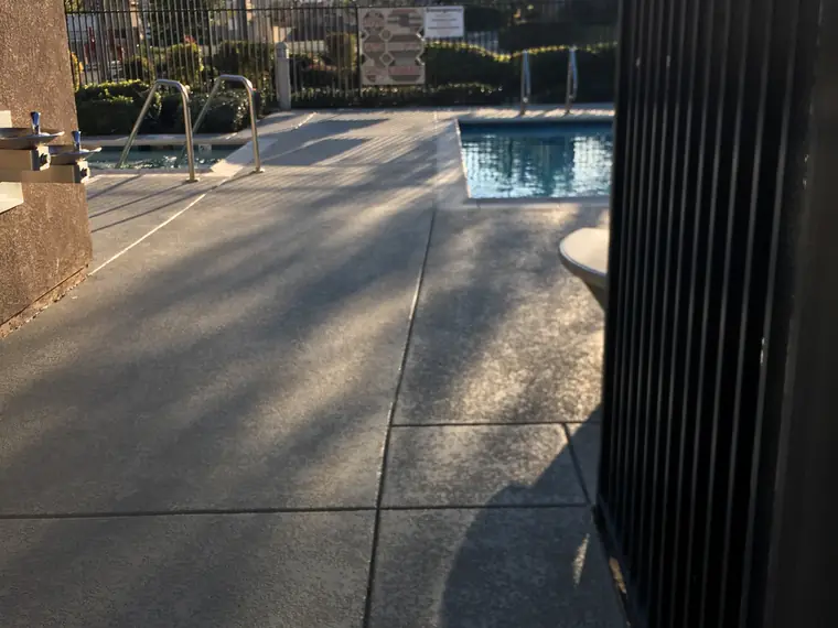 Gray textured pool deck with a dark blue-gray border seen from the gate