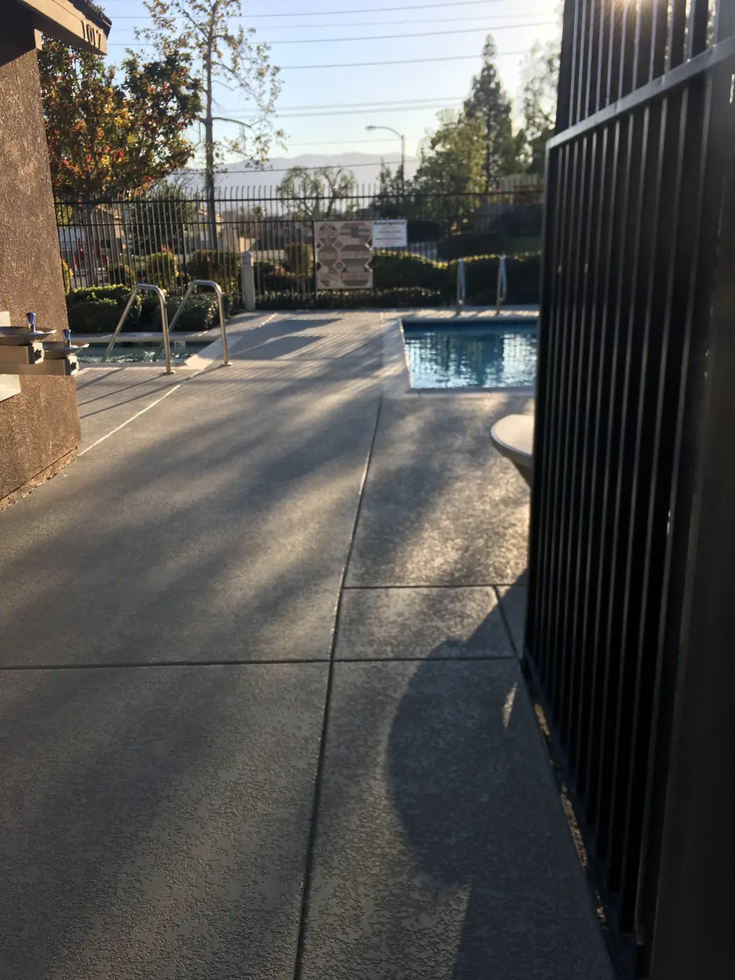 Gray textured pool deck with a dark blue-gray border seen from the gate