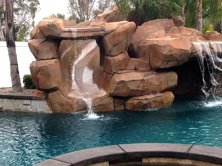 Terracotta faux rock waterfall feature above a clear blue pool