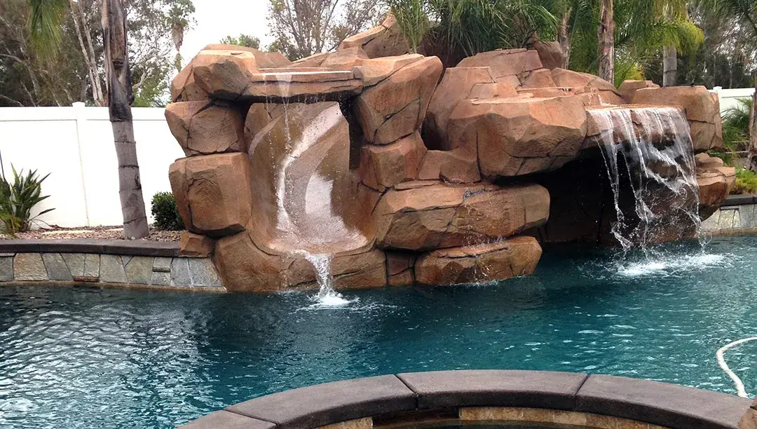 Terracotta faux rock waterfall feature above a clear blue pool