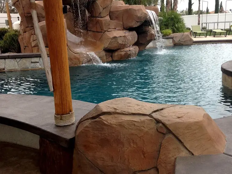 Rock waterfall and palapa post beside a swimming pool