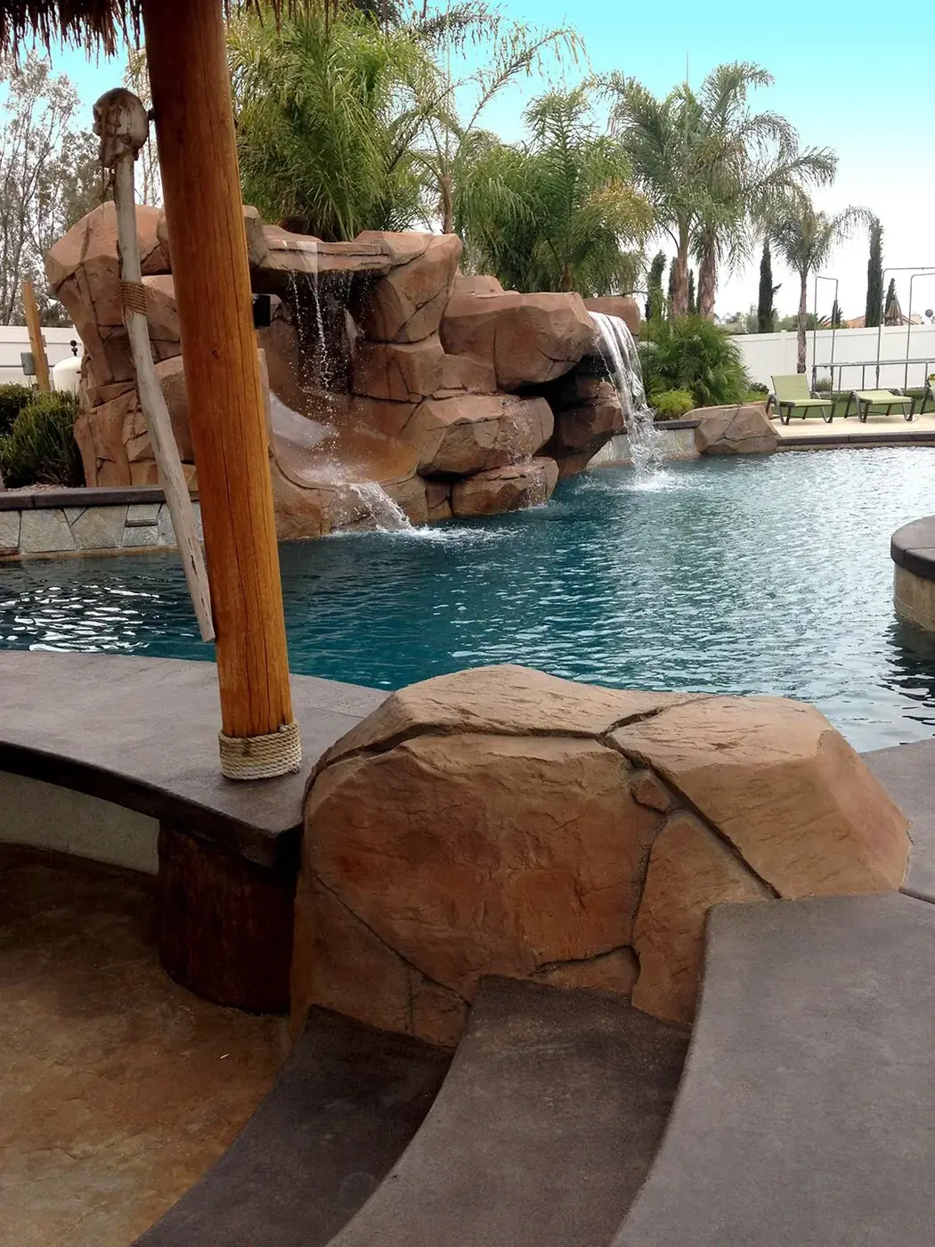 Rock waterfall and palapa post beside a swimming pool