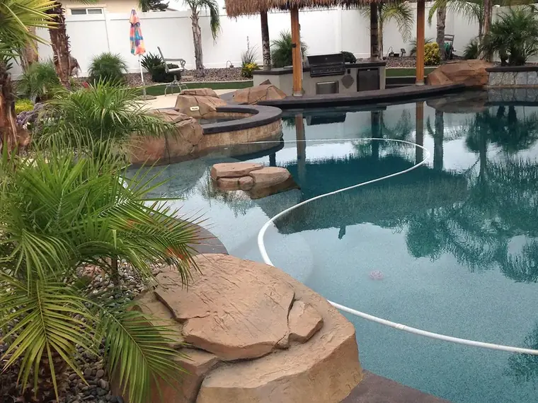 Backyard pool with restained boulders and a thatched palapa