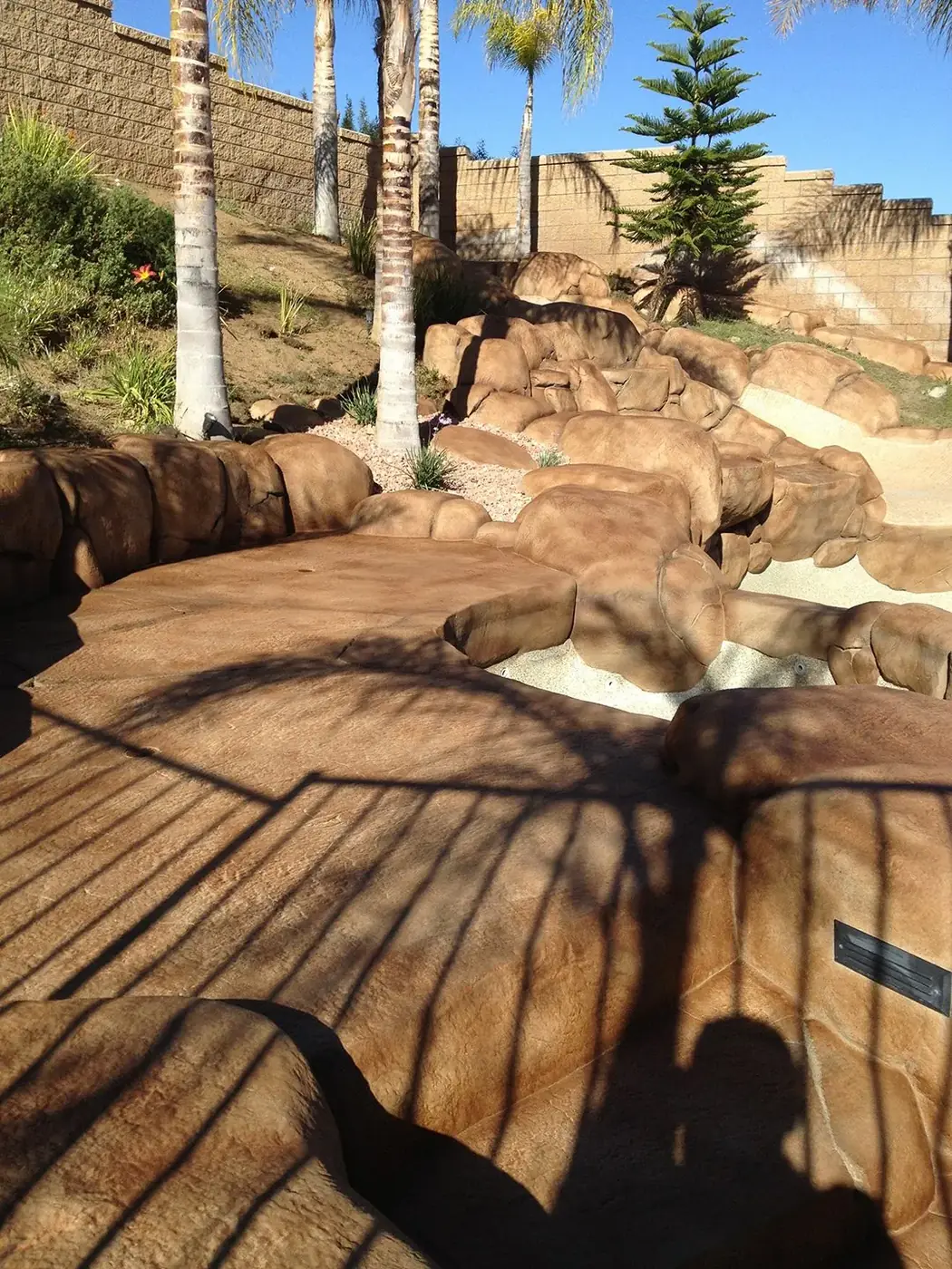 Restained rock feature and stained deck under palm shadow