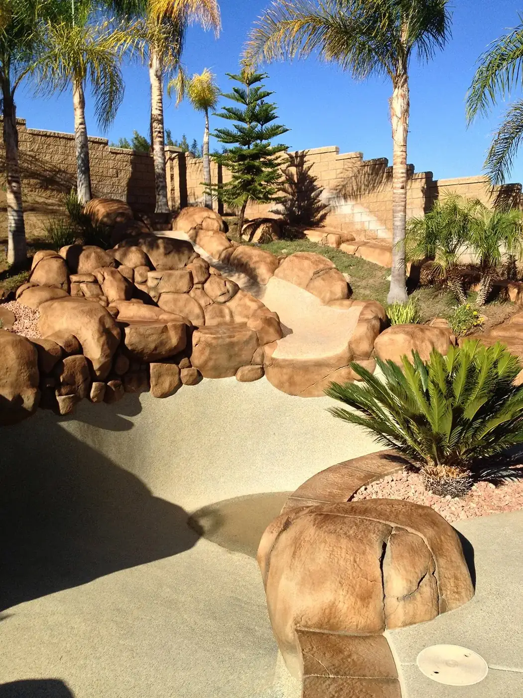 Restained boulder retaining wall with palms and desert planting