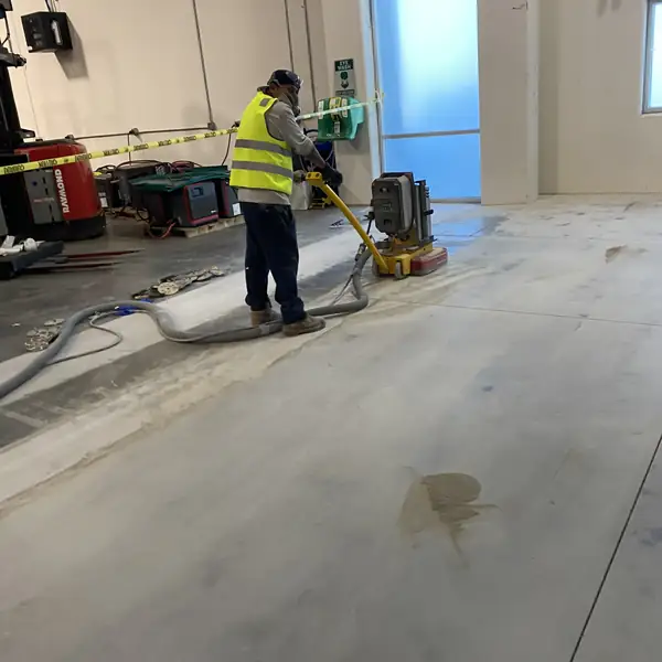 Worker in a high-visibility vest running a grinder across an interior concrete floor