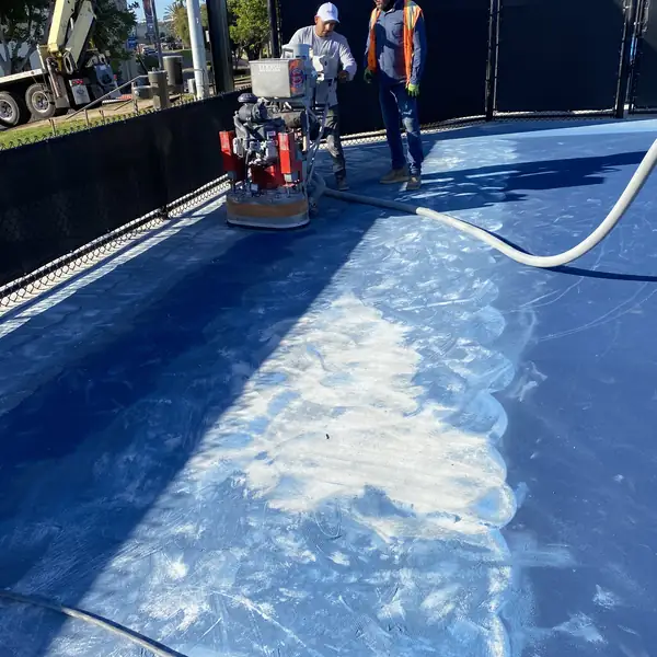 Crew grinding the blue surface off a pickleball court in bright sun