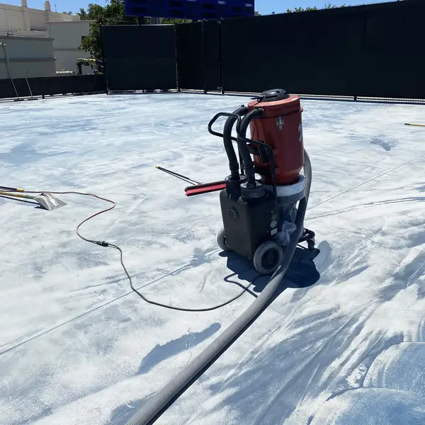 Walk-behind grinder and hose on a court stripped back to gray concrete