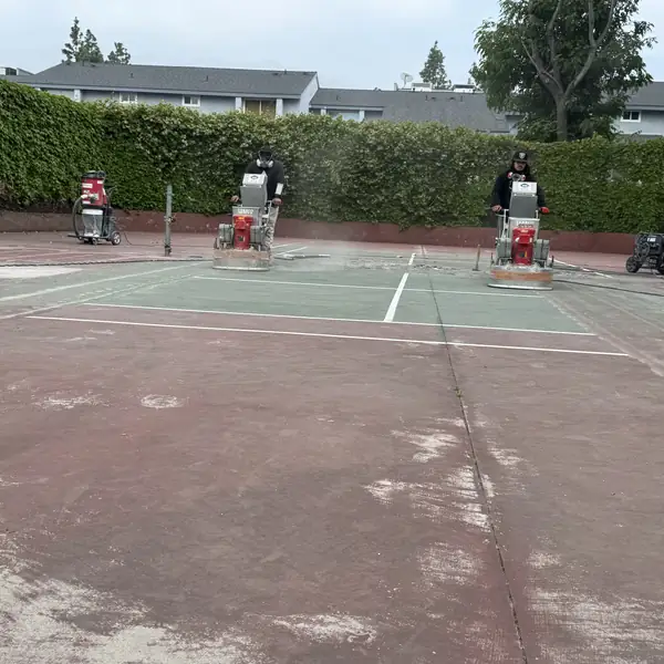 Green painted tennis court with white lines and grinding machines set up along the baseline
