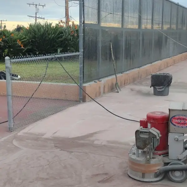 Grinding equipment on a court beside a chain link fence and lawn