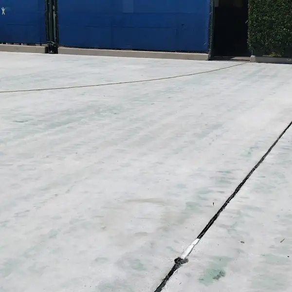 Court surface ground back to clean gray concrete against a blue wall