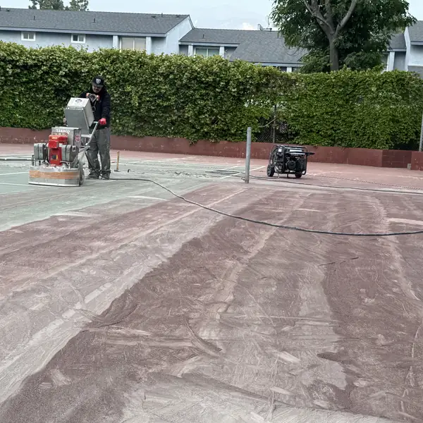Worker grinding the red surface off a tennis court in front of apartments