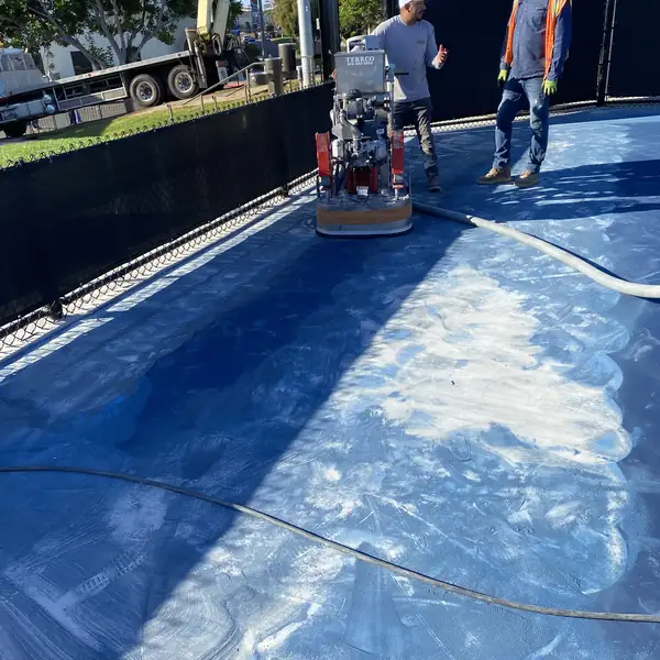 Grinder cutting a pale stripe through the blue coating on a sports court