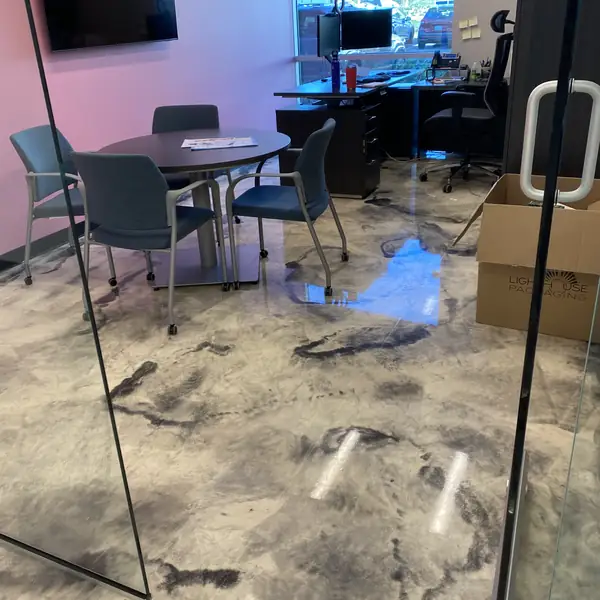 Metallic epoxy floor reflecting the ceiling lights beside a glass meeting room