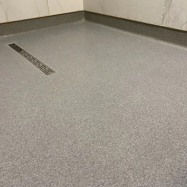 Gray flake epoxy floor with a stainless trench drain and coved wall base