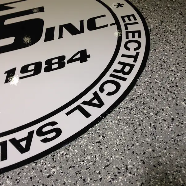 Close view of an electrical company logo inlaid into a gray flake epoxy floor