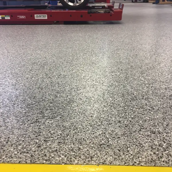 Gray flake epoxy floor beneath a wheel alignment rack in a service shop