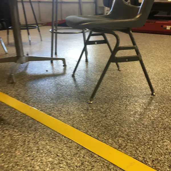 Olive flake epoxy shop floor with a yellow boundary line and a work chair