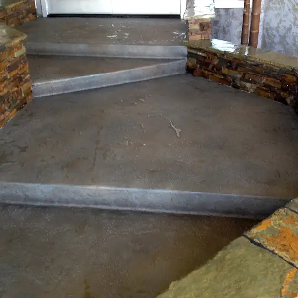 Gray and brown stained entry steps beside a stone-faced planter