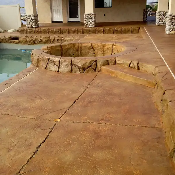 Brown stained and scored patio beside a pool with rock coping
