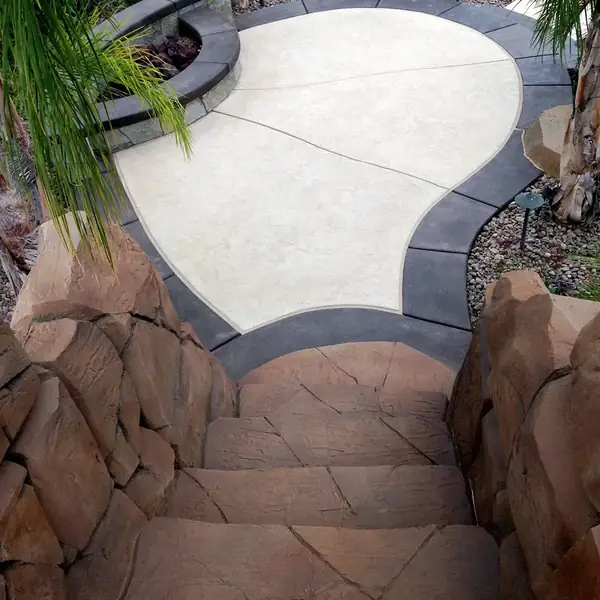 Cream and gray stained deck curving between rock features and a pool