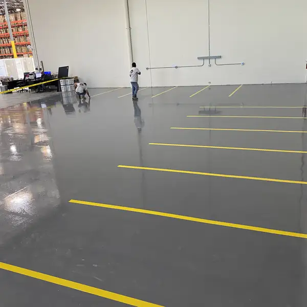 Gray epoxy warehouse floor marked out with yellow aisle striping while crews work at the far wall